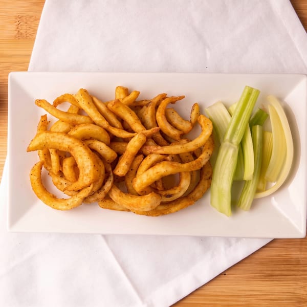 A white rectangular plate holds golden curly fries and fresh celery sticks on a white napkin.