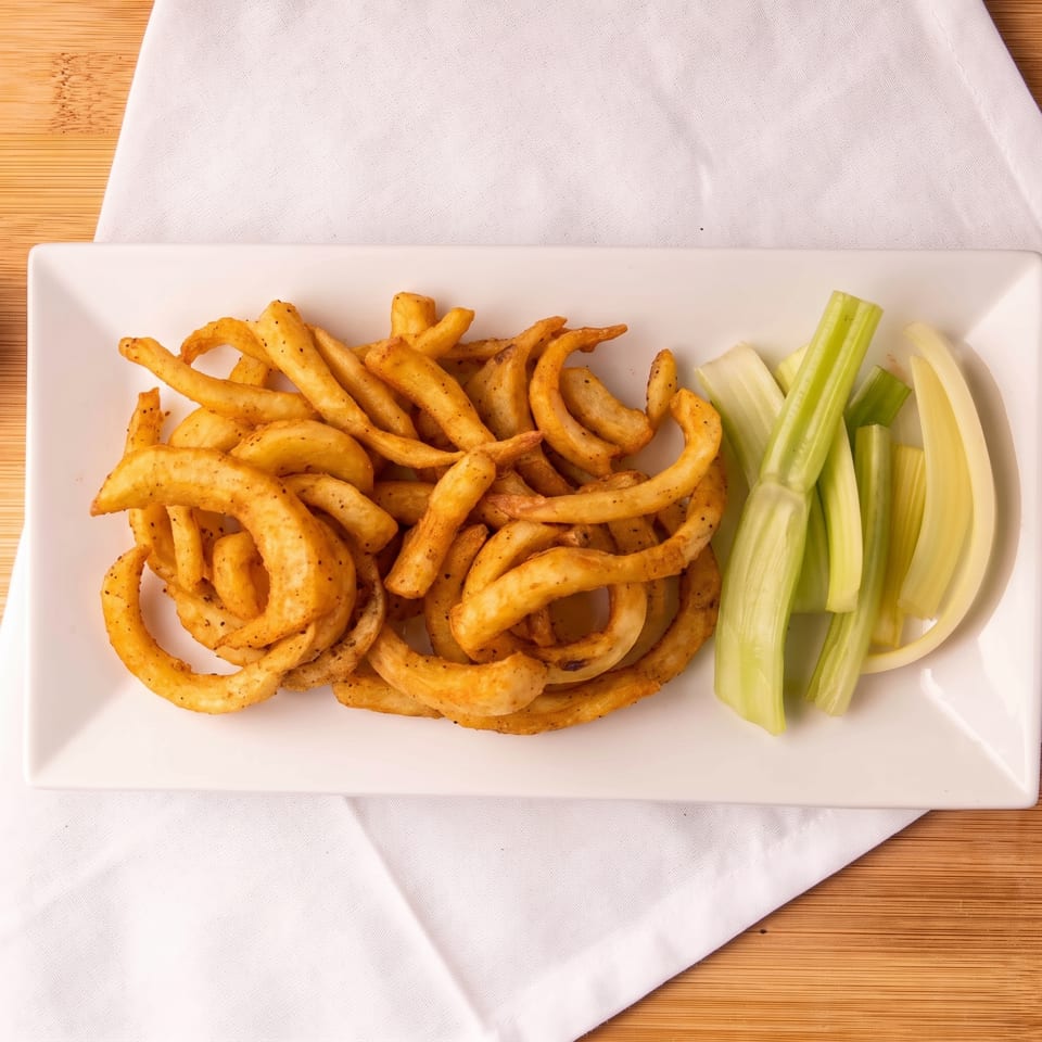 A white rectangular plate holds golden curly fries and fresh celery sticks on a white napkin.
