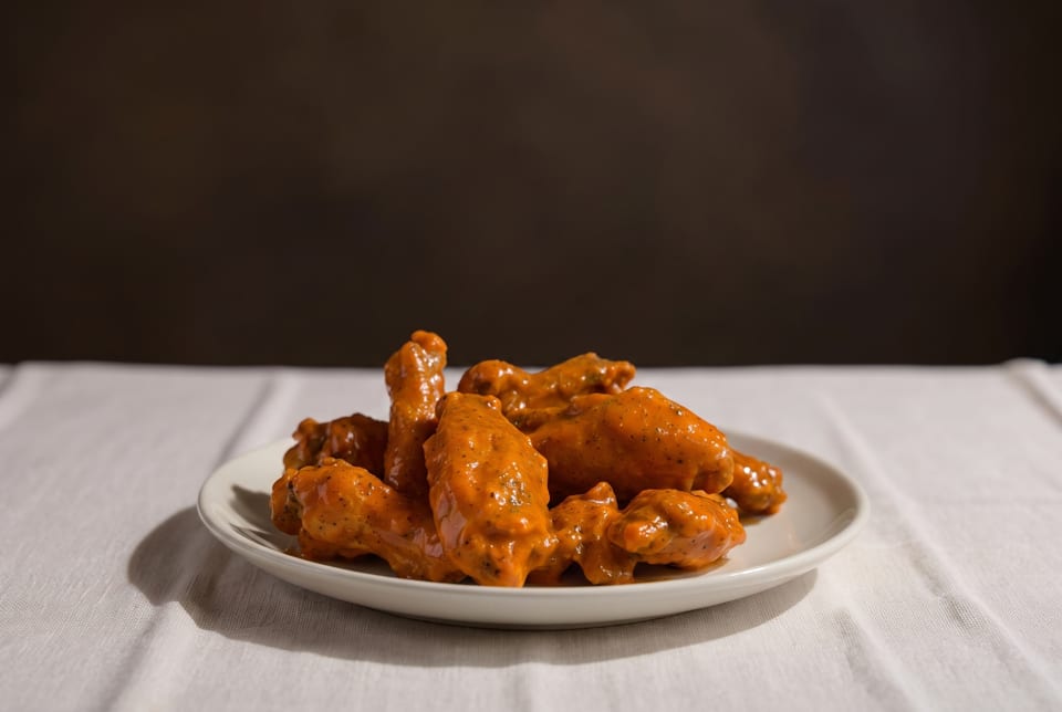 A white plate piled high with buffalo chicken wings, coated in a rich orange sauce.